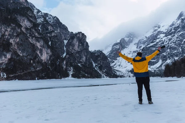 Adam kış boyunca Alp dağlarının ortasında Di Braies gölünde kollarını kaldırıyor.