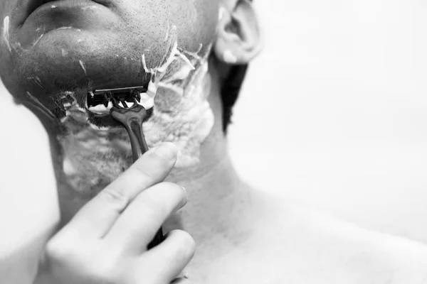 A man is shaving a machine, a cheek in foam, close-up. Bristles