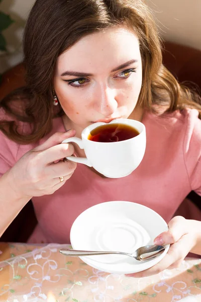 Μια νεαρή γυναίκα πίνει τσάι από ένα λευκό φλιτζάνι κοντά στο παράθυρο. — Φωτογραφία Αρχείου