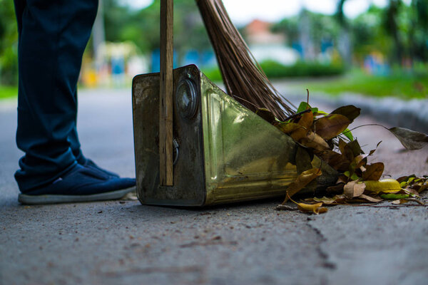 An Asian woman is sweeping dry leaves by the road in the outdoor