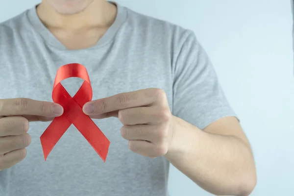 Ayuda a la conciencia, manos masculinas sosteniendo cinta roja de la conciencia del SIDA. Wo. — Foto de Stock