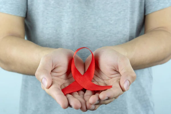 Ayuda a la conciencia, manos masculinas sosteniendo cinta roja de la conciencia del SIDA. Wo. — Foto de Stock