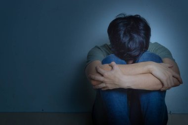 Üzgün adam, karanlık bir odada tek başına otururken dizine sarılıp ağlar. Sefalet