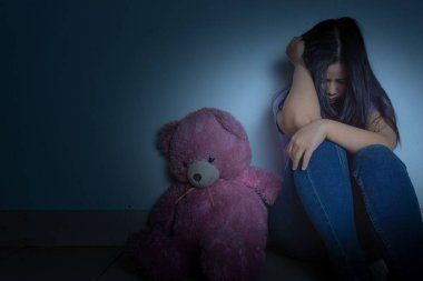 Üzgün kadın dizine sarıldı ve ağladı. Karanlıkta oyuncak ayıyla otururken.