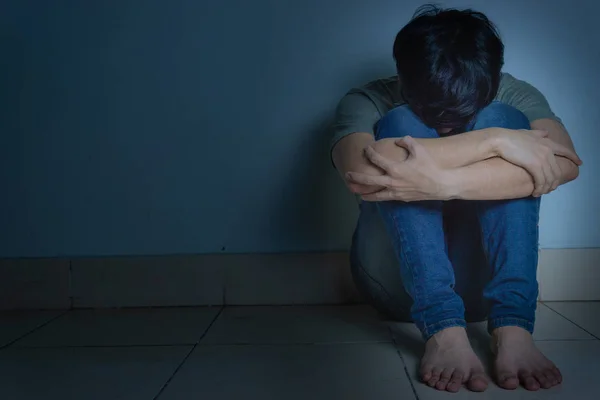 Homem triste abraçar o joelho e chorar sentado sozinho em um quarto escuro. Depre — Fotografia de Stock