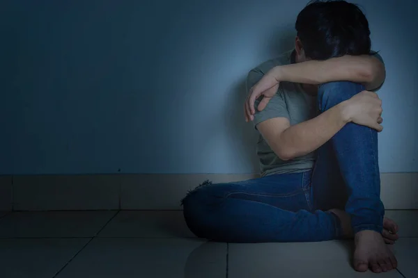 Üzgün adam, karanlık bir odada tek başına otururken dizine sarılıp ağlar. Sefalet