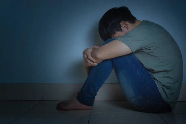 Homem triste abraçar o joelho e chorar sentado sozinho em um quarto escuro. Depre — Fotografia de Stock