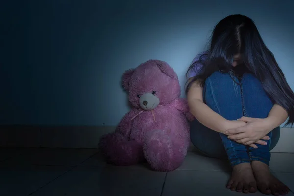 Sad woman hug her knee and cry sitting with teddy bear in a dark — Stock Photo, Image