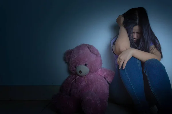 Triste donna abbracciare il ginocchio e piangere seduto con orsacchiotto in un buio — Foto Stock