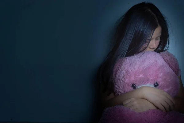 Sad woman hug her knee and cry sitting with teddy bear in a dark — Stock Photo, Image