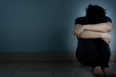 Üzgün adam, karanlık bir odada tek başına otururken dizine sarılıp ağlar. Sefalet