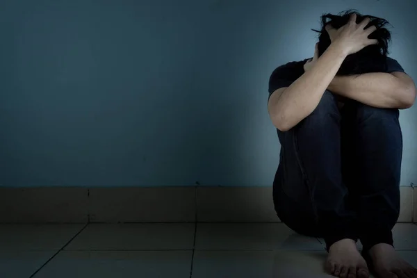 Triste hombre abrazar su rodilla y llorar sentado solo en un cuarto oscuro. Depre. — Foto de Stock