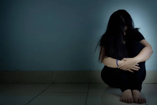 Грустная женщина обнимает колено и плачет, сидя одна в темной комнате. Деп — стоковое фото