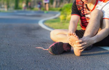 Genç adam koşmaktan ve koşmaktan acılı ayağına masaj yapıyor.