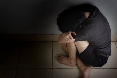 Üzgün adam, karanlık bir odada tek başına otururken dizine sarılıp ağlar. Sefalet