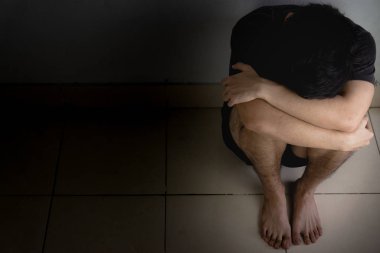 Üzgün adam, karanlık bir odada tek başına otururken dizine sarılıp ağlar. Sefalet