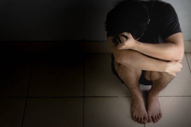 Üzgün adam, karanlık bir odada tek başına otururken dizine sarılıp ağlar. Sefalet