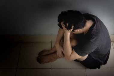 Üzgün adam, karanlık bir odada tek başına otururken dizine sarılıp ağlar. Sefalet