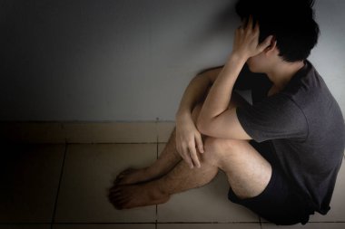 Üzgün adam, karanlık bir odada tek başına otururken dizine sarılıp ağlar. Sefalet