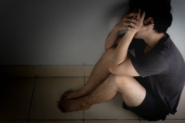 Üzgün adam, karanlık bir odada tek başına otururken dizine sarılıp ağlar. Sefalet