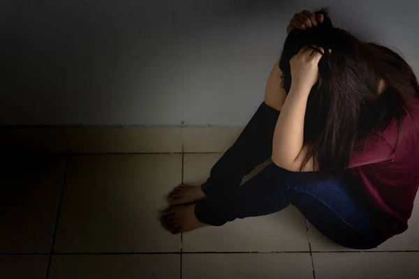 Mujer triste abrazar su rodilla y llorar sentado solo en una habitación oscura. Dep. —  Fotos de Stock