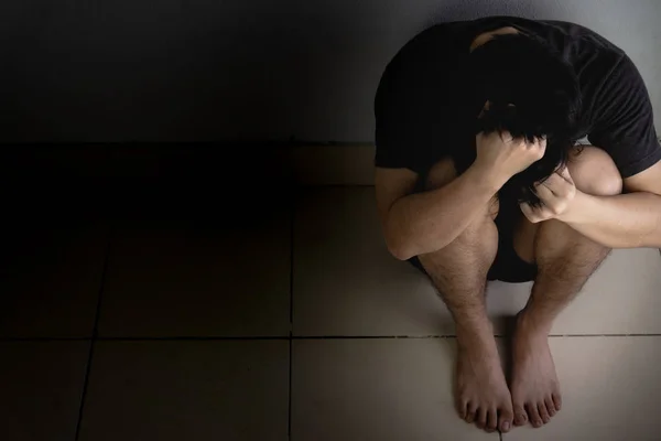 Homem triste abraçar o joelho e chorar sentado sozinho em um quarto escuro. Depre — Fotografia de Stock