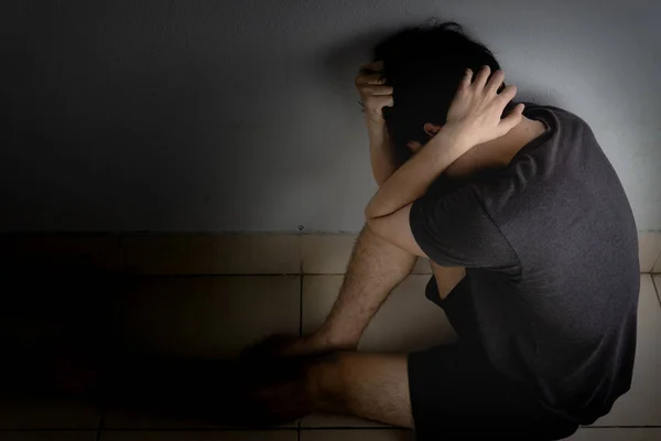 Homem triste abraçar o joelho e chorar sentado sozinho em um quarto escuro. Depre — Fotografia de Stock