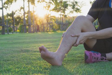 Genç bir adam parkta koşmaktan ve koşmaktan dolayı ağrılı baldırına masaj yapıyor. Spor ve egzersiz konsepti.
