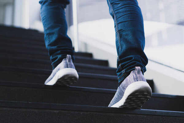 close up legs of young businessman while walking up the stairs in the modern city with the sunspot background. Go up, success, grow up concept.