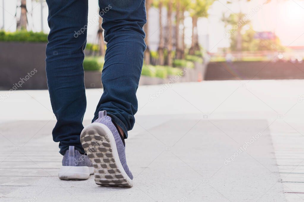 close up legs of young businessman while walking forward in the modern city with the sunspot background. Go up, success, grow up concept.