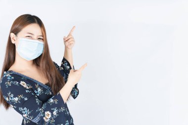 Koronavirüsü korumak için tıbbi koruma maskesi takan Asyalı güzel mutlu hippi kadın, başbakanın tozunu filtrele 2,5 ve soğuk ve parmağını beyaz arka planı işaret ediyor.