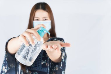 Koronavirüsü korumak için tıbbi koruma maskesi takan Asyalı güzel mutlu hipster kadın, başbakanın tozunu filtrele 2,5 ve soğuk ve beyaz arka planda dezenfektan el jeli kullanıyor.