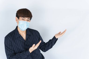 Koronavirüsü korumak için tıbbi koruma maskesi takan Asyalı yakışıklı hippi adam, başbakanı filtre tozu 2.5 ve soğuk ve beyaz arka planı işaret eden parmağı