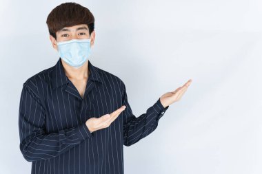 Koronavirüsü korumak için tıbbi koruma maskesi takan Asyalı yakışıklı hippi adam, başbakanı filtre tozu 2.5 ve soğuk ve beyaz arka planı işaret eden parmağı