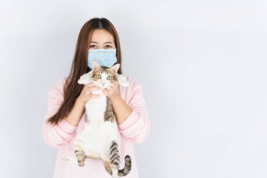 Koronavirüsü korumak için tıbbi koruma maskesi takan Asyalı güzel mutlu kadın başbakan 2.5 numaralı filtre tozu, kedi kürküne alerjisi var ve beyaz arka planda bir kedi taşıyor.
