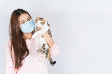 Koronavirüsü korumak için tıbbi koruma maskesi takan Asyalı güzel mutlu kadın başbakan 2.5 numaralı filtre tozu, kedi kürküne alerjisi var ve beyaz arka planda bir kedi taşıyor.