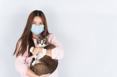 Koronavirüsü korumak için tıbbi koruma maskesi takan Asyalı güzel mutlu kadın başbakan 2.5 numaralı filtre tozu, kedi kürküne alerjisi var ve beyaz arka planda bir kedi taşıyor.