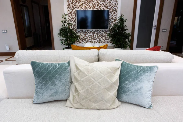 Almohadas azules y blancas en un sofá blanco, salón interior. Un televisor blanco está colgando en la pared. — Foto de Stock