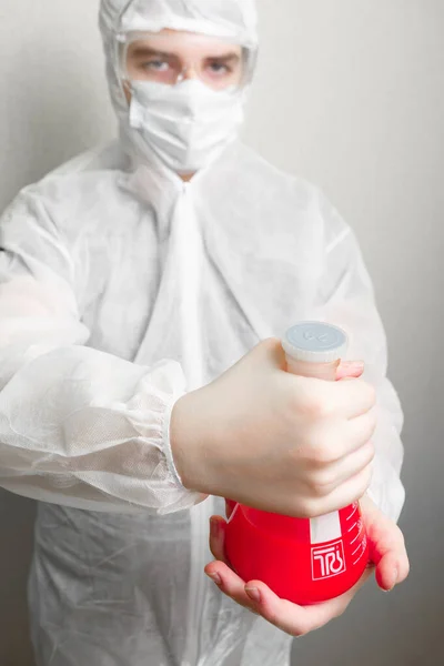 2020年世界大流行性结肠炎 对抗结肠癌病毒的科学在框架中 一名穿着白色西装 帽子和面具的实验室助理 手里拿着瓶红色液体 象征着结肠炎病毒 酒瓶在前排 — 图库照片