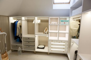 Giysiler için soyunma odasında bej bir gardırop. Rafları aç, eşyalar askıda asılı kalsın. Raflarda, terazilerde, demirde, ilk yardım çantasında, askılarda..