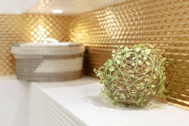 Ön planda yapay dekoratif yeşil bitki var. Oda dekorasyonu. Arka planda bulanık bir sepet rafta duruyor. Duvarlar altınla süslenmiş..