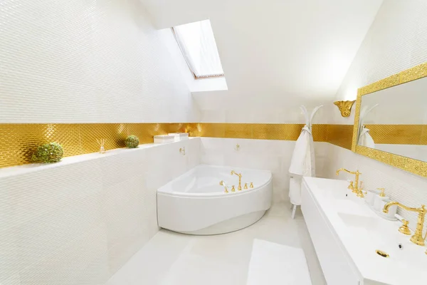 White bathroom with gold trim. Corner bathroom, chic mirror with washbasin. Lamps trimmed with gold. Bathrobe and towels on a hanger. White floor mat.
