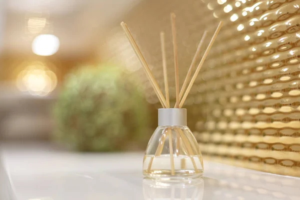 stock image Air fragrance, essential oils and sticks. Room decor element. Artificial ornamental green plant and wicker basket in the background in blur. The walls are decorated with gold.