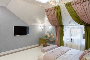 Yatak odası parlak renklerde. Pencerenin üzerinde yeşil-pembe perdeler var. Duvarda beyaz bir televizyon var. Aynalı giyinme masası. Yeşil bir koltuk. Ataman 'la yatak. Avize parlıyor..