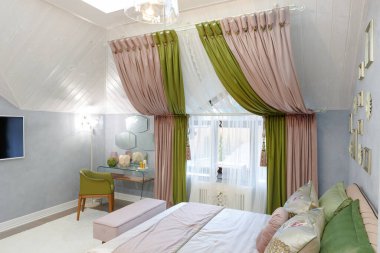 Yatak odası parlak renklerde. Pencerenin üzerinde yeşil-pembe perdeler var. Duvarda beyaz bir televizyon var. Aynalı giyinme masası. Yeşil bir koltuk. Ataman 'la yatak. Avize parlıyor..