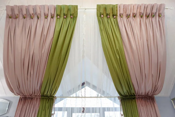 Beautiful curtains on the window under the ceiling. Green-pink curtains, white tulle on the window.