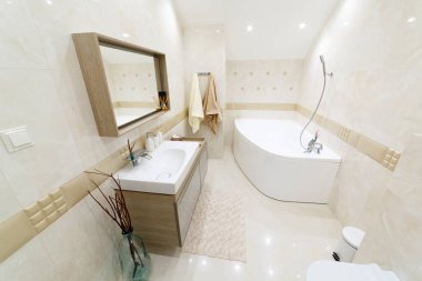 Altın kaplamalı beyaz banyo. Köşedeki banyo, lavabolu şık bir ayna. Altınla süslenmiş lambalar. Bornoz ve havlular askıda. Beyaz zemin paspas.