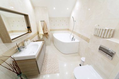 Altın kaplamalı beyaz banyo. Köşedeki banyo, lavabolu şık bir ayna. Altınla süslenmiş lambalar. Bornoz ve havlular askıda. Beyaz zemin paspas.
