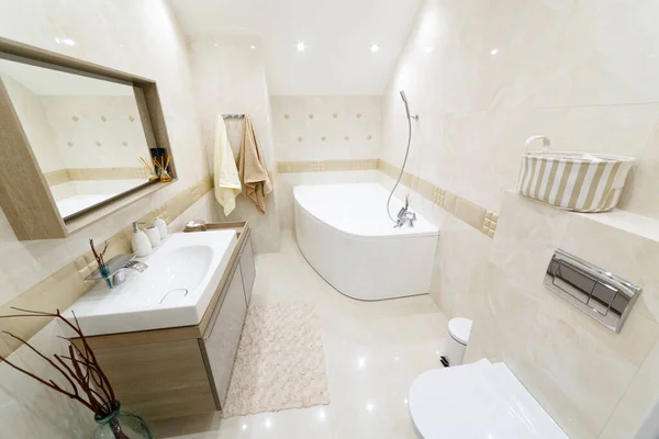 White bathroom with gold trim. Corner bathroom, chic mirror with washbasin. Lamps trimmed with gold. Bathrobe and towels on a hanger. White floor mat.
