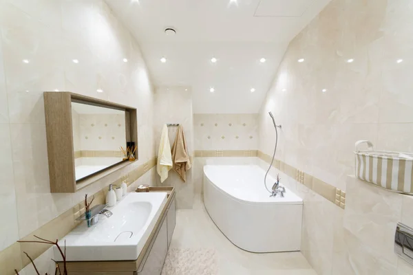 White bathroom with gold trim. Corner bathroom, chic mirror with washbasin. Lamps trimmed with gold. Bathrobe and towels on a hanger. White floor mat.